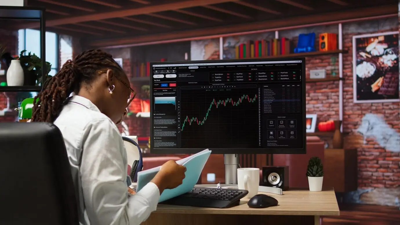 Ein Daytrader, der am Computer Aktien kauft und verkauft und dabei Dokumente durchsieht.