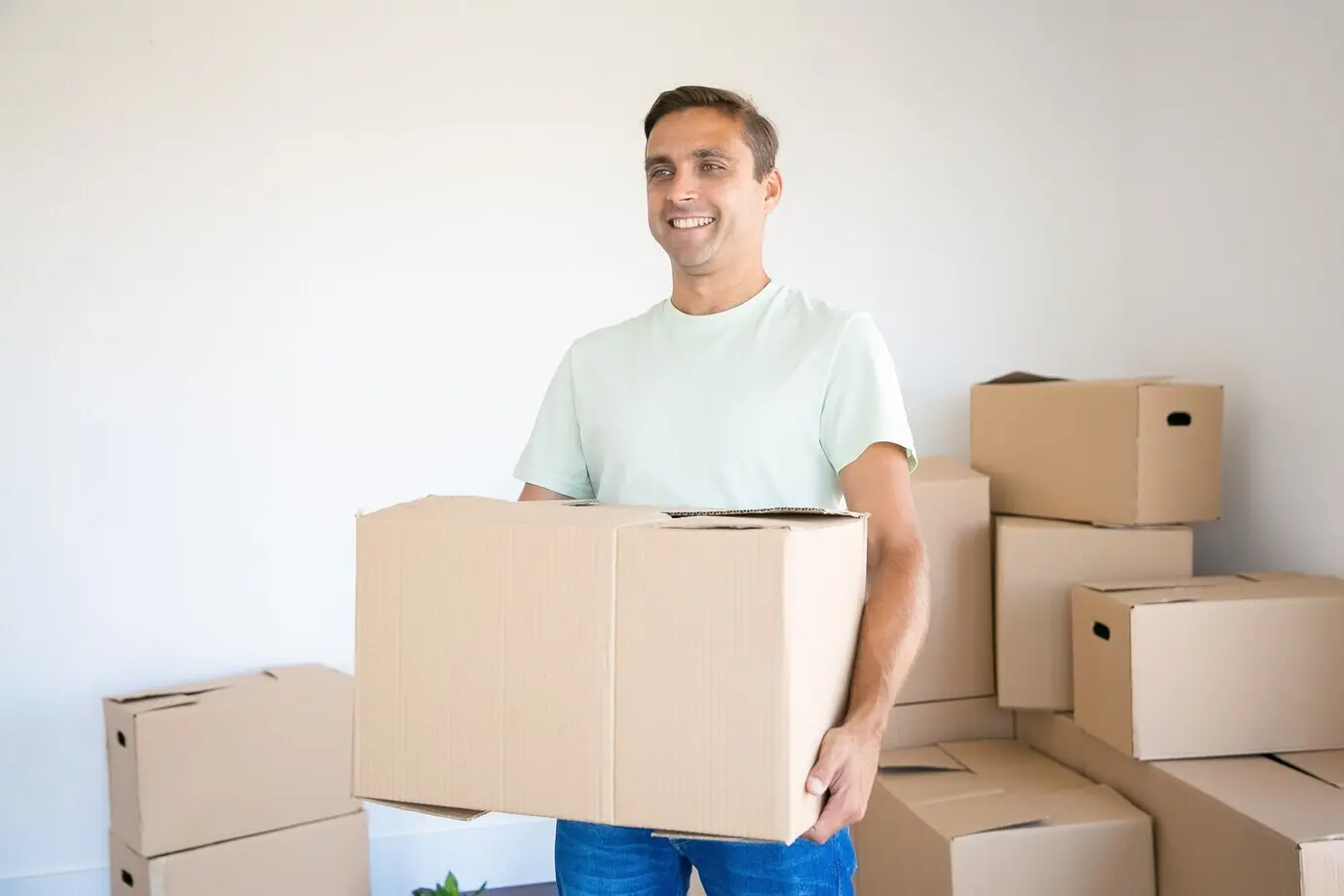 Kaukasischer Mann, der einen Pappkarton in seinem neuen Haus oder seiner neuen Wohnung trägt.